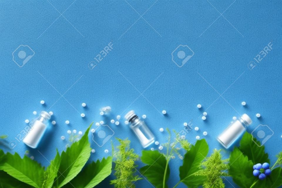 Fondo del borde de la homeopatía, glóbulos en botellas y hierbas sobre fondo azul. Naturopatía y medicina alternativa