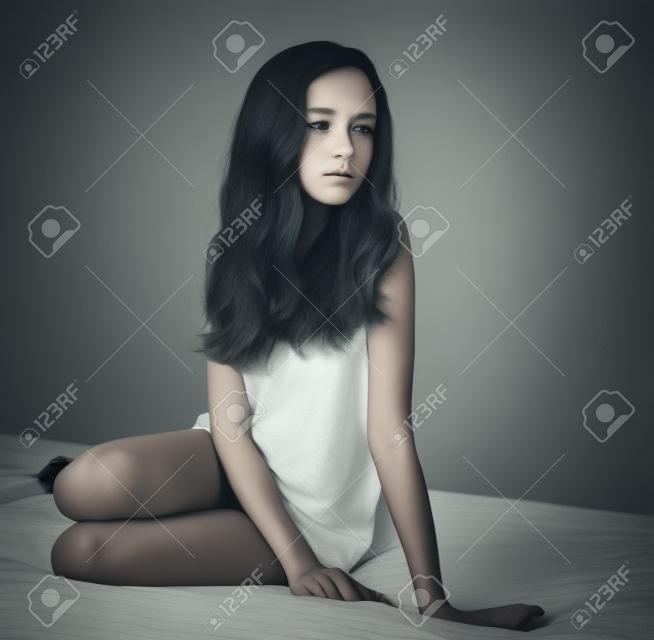 tinted image sad girl sitting on the bed and looking away. square format