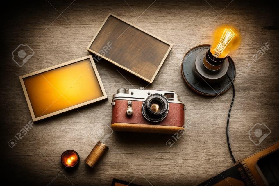 Vintage photo camera. Blank photo frames. Retro lamp light bulb. Old album and camera rolls. Wooden rustic background.
