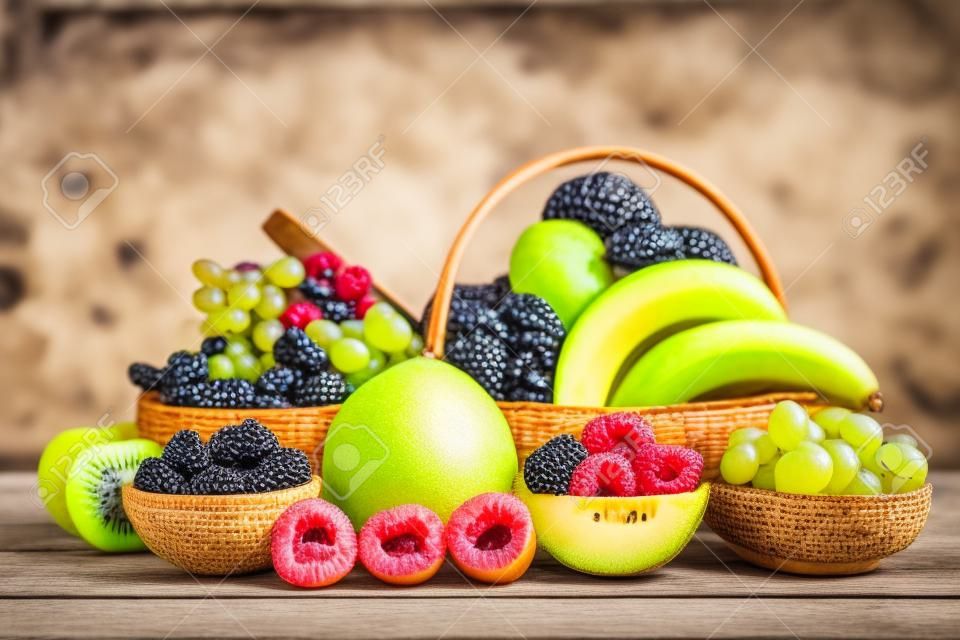 Gruppe Gesundes frisches Obst in einem Holzkorb, mit Vitaminen c aus Bananen, Kiwi, Trauben, Himbeeren, Blaubeeren und Brombeeren, gut für den Körper und Diätkost auf dem Tisch im Naturhintergrund.