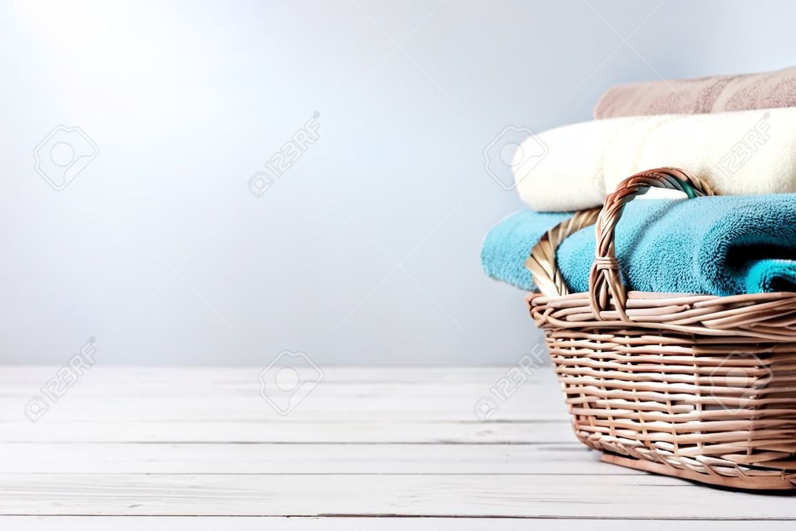 Toalhas de banho de cores diferentes na cesta de vime no fundo claro