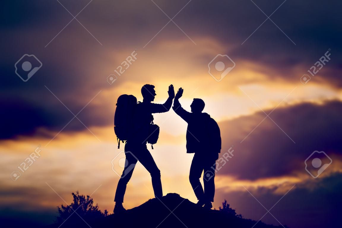 Hiking people reaching summit top giving high five at mountain top at sunset