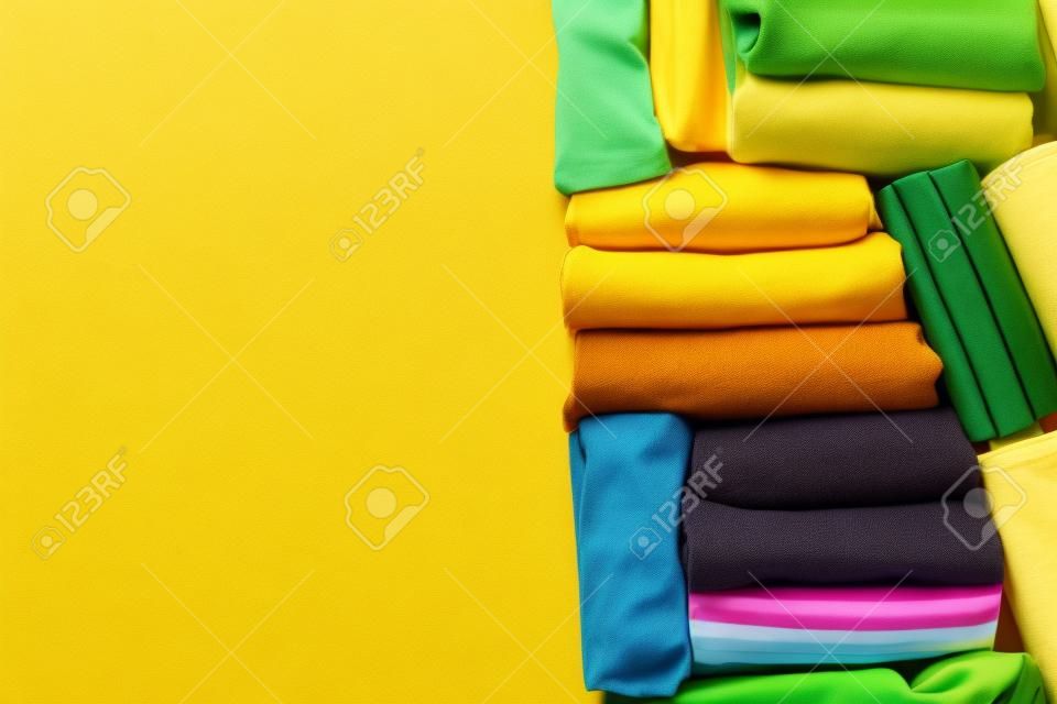 close up of rolled colorful t shirt clothes on yellow table background, travel concept