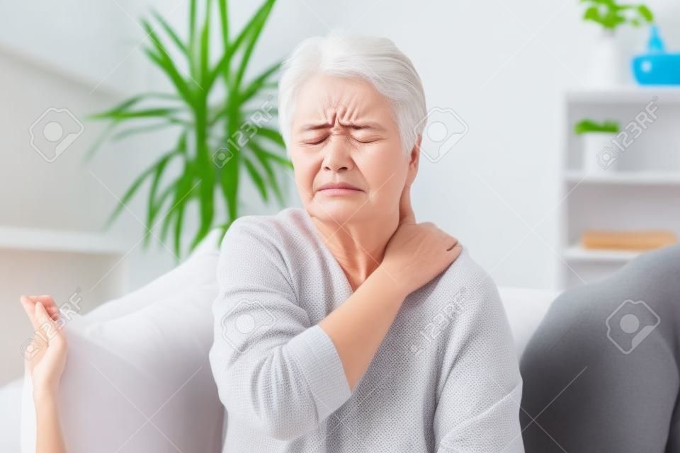 Infeliz 60 anos de idade mulher massageando pescoço em casa, sofrendo de dor severa nas costas. sensação feminina sênior mal-estar nos músculos cansados, conceito de problema de saúde