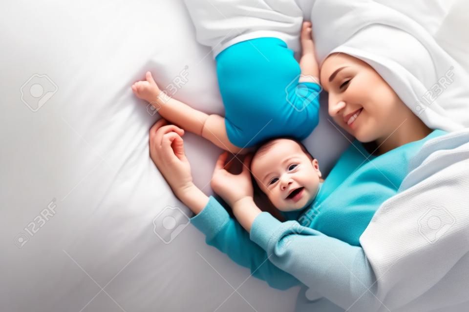 Happy mother with baby lying together on bed at home