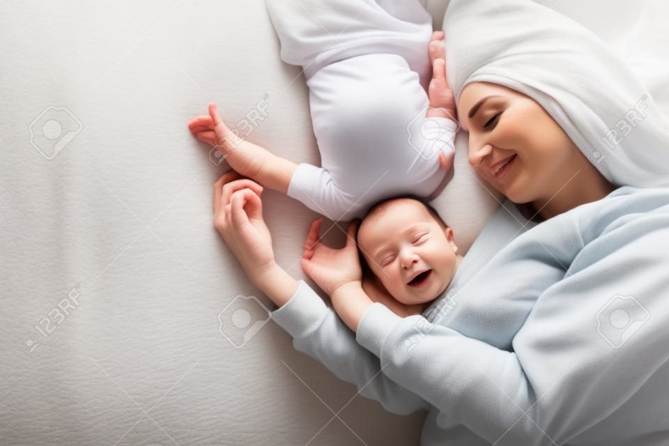 Gelukkige moeder met baby liggen samen op bed thuis