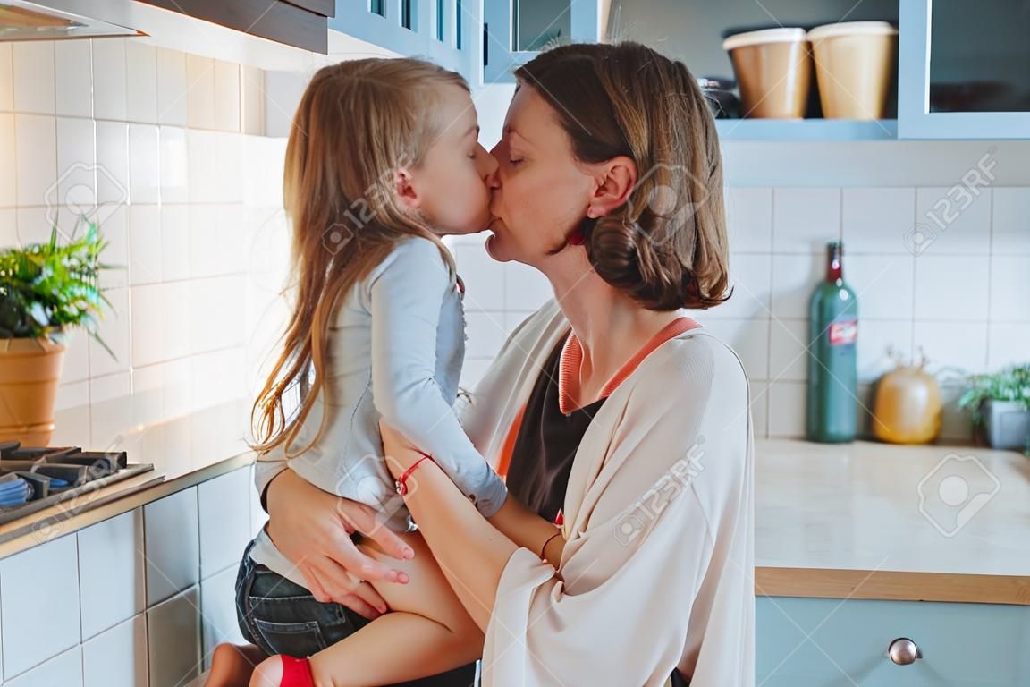 Mom kisses her little daughter in the kitchen