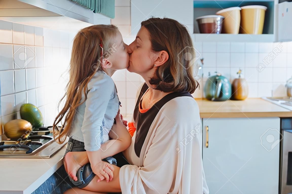 Mom kisses her little daughter in the kitchen