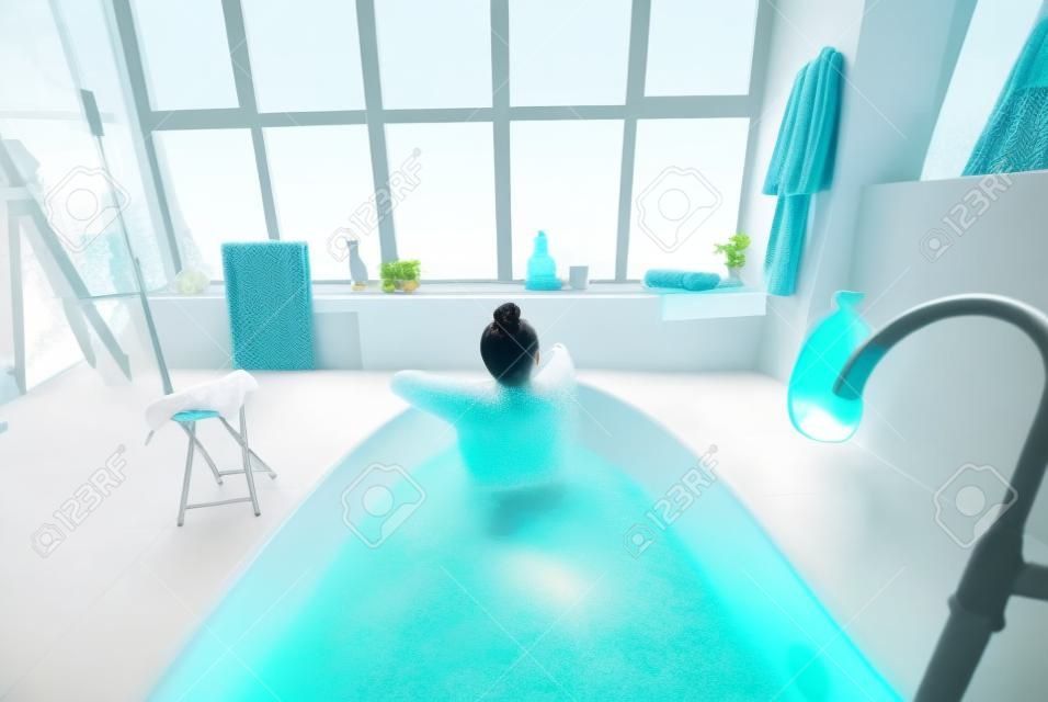 Relaxed lady taking bath, enjoying and relaxing while lying in bathtub, back view