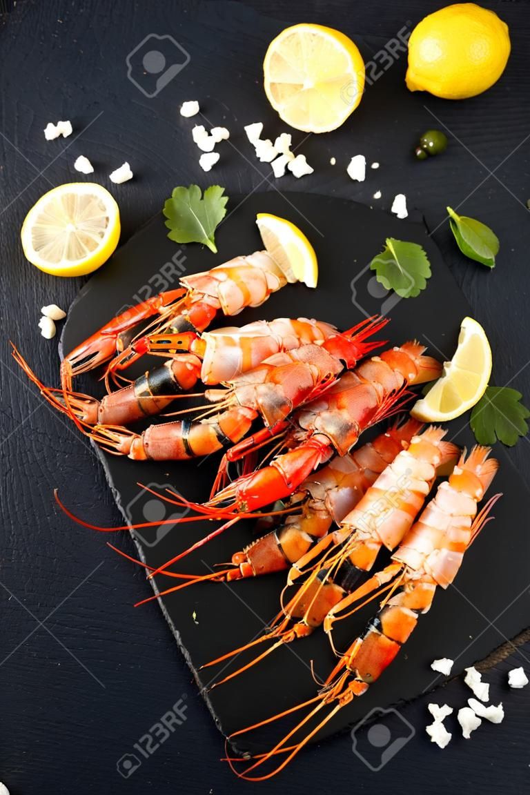 langoustines with spices, lemon and herbs on a black background. Tiger prawns with spices and lemon. Top view.