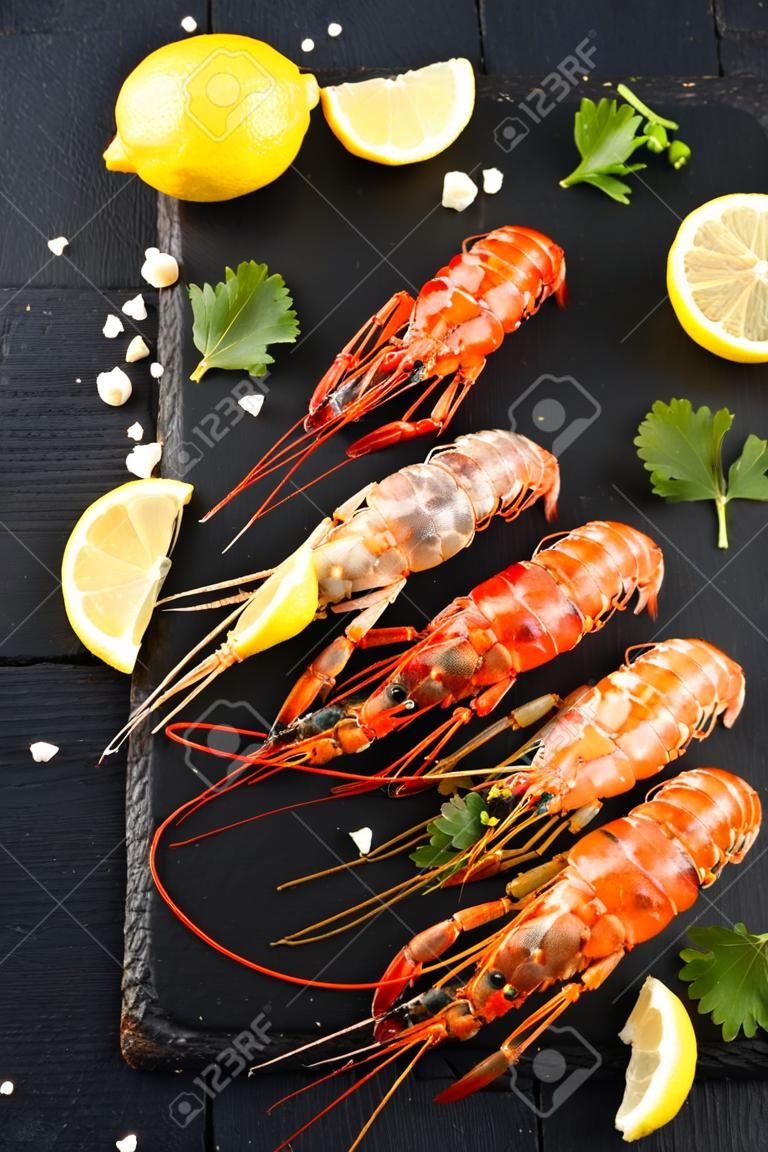 langoustines with spices, lemon and herbs on a black background. Tiger prawns with spices and lemon. Top view.