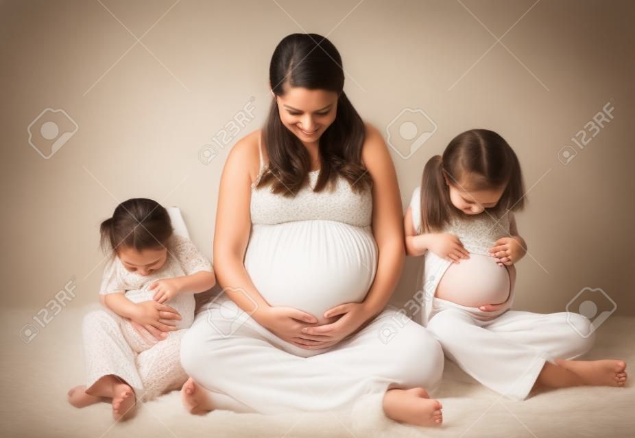 Portrait de maternité d'une maman enceinte et ses deux filles regardent tous leurs ventres