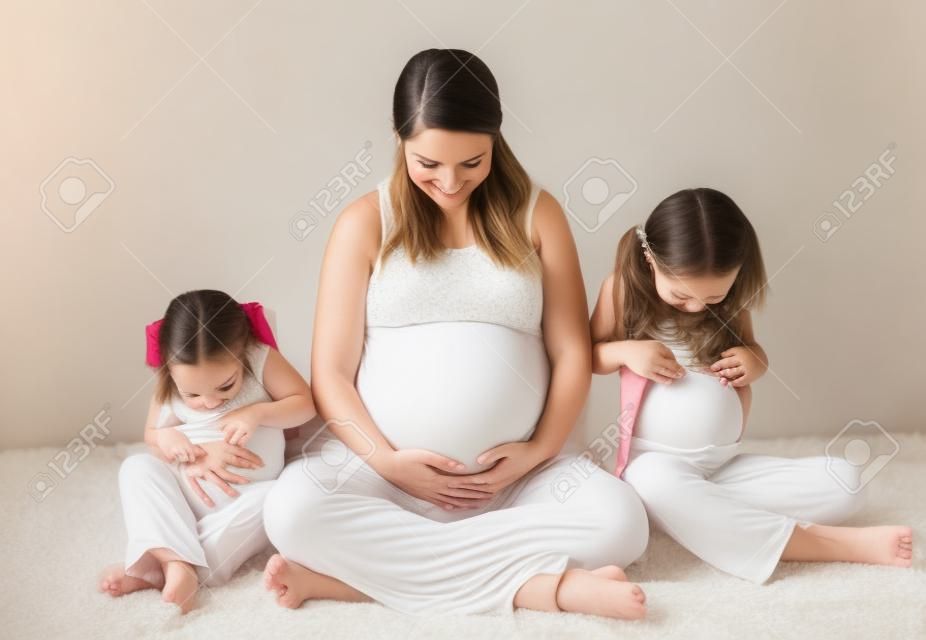 Portrait de maternité d'une maman enceinte et ses deux filles regardent tous leurs ventres