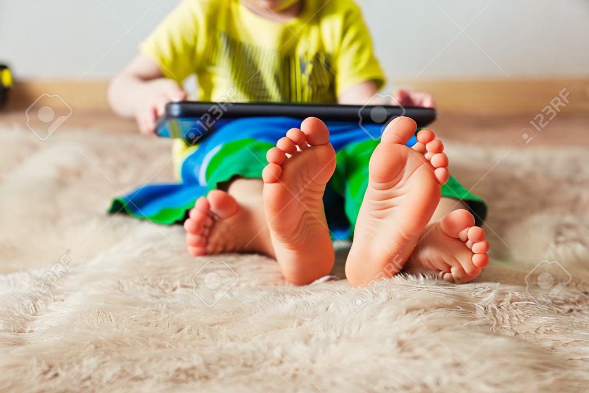 kid avec tablette assis sur le lit et en regardant la caméra. mise au point sélective sur le lit. mignon garçon dans un t-shirt vert et un pantalon vert