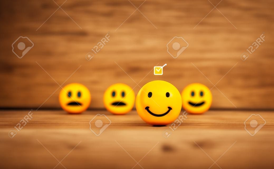 Marque una casilla de verificación en la cara de emoticono sonriente en las bolas de madera sobre fondo oscuro. Concepto de evaluación, calificación, retroalimentación y encuesta de satisfacción del servicio al cliente.