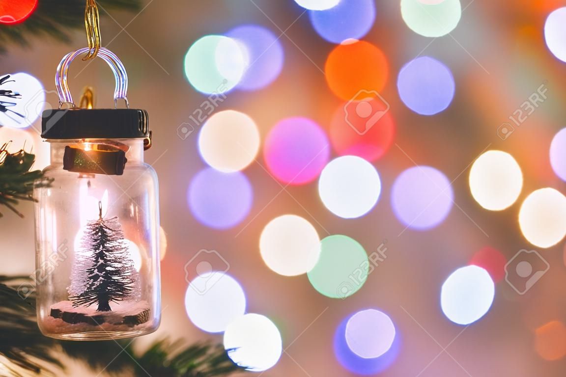 Weihnachtsdekoration. Hängender kleiner Weihnachtsbaum im Glas auf Tannenzweigen Weihnachtsbaumgirlande und Ornamente über abstraktem Bokeh