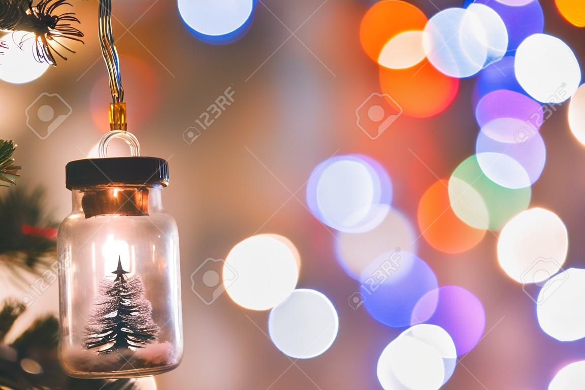 Weihnachtsdekoration. Hängender kleiner Weihnachtsbaum im Glas auf Tannenzweigen Weihnachtsbaumgirlande und Ornamente über abstraktem Bokeh
