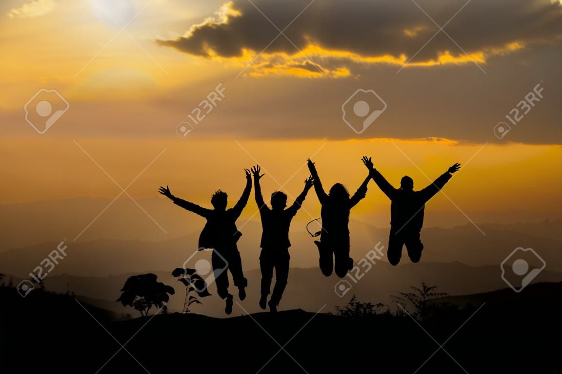 Gruppo di persone felici che saltano in montagna al tramonto, concetto di divertirsi sulla collina, silhouette