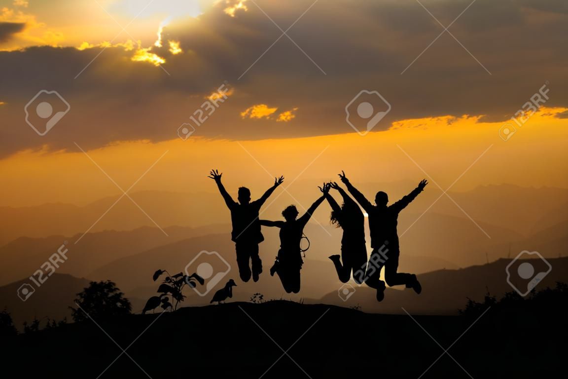 Gruppo di persone felici che saltano in montagna al tramonto, concetto di divertirsi sulla collina, silhouette