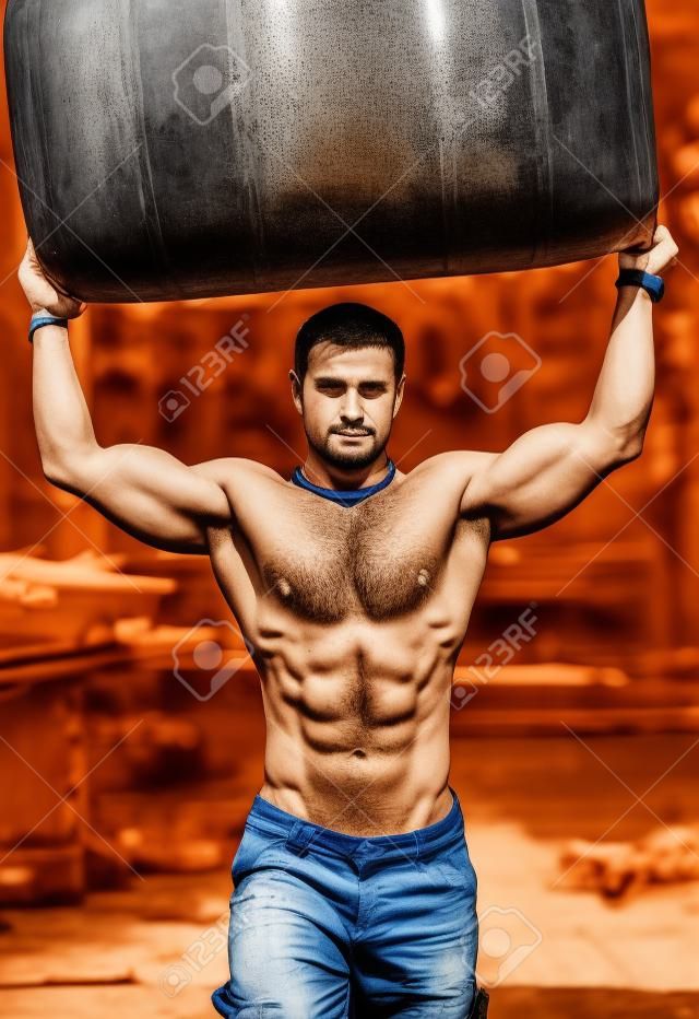 Hot, shirtless, muscular construction worker carrying big barrel over his head