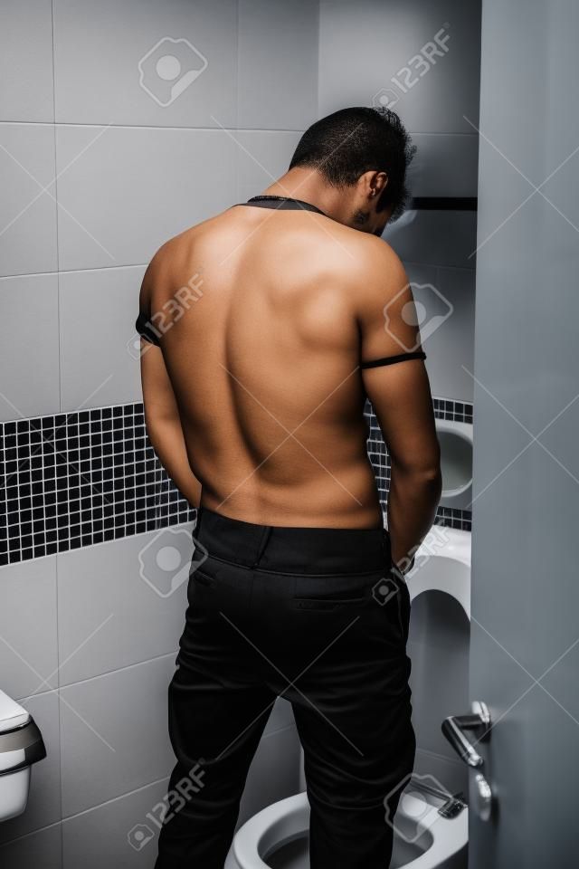Vista posterior de un hombre joven en traje Negro Orinar en el aseo interior de su baño.
