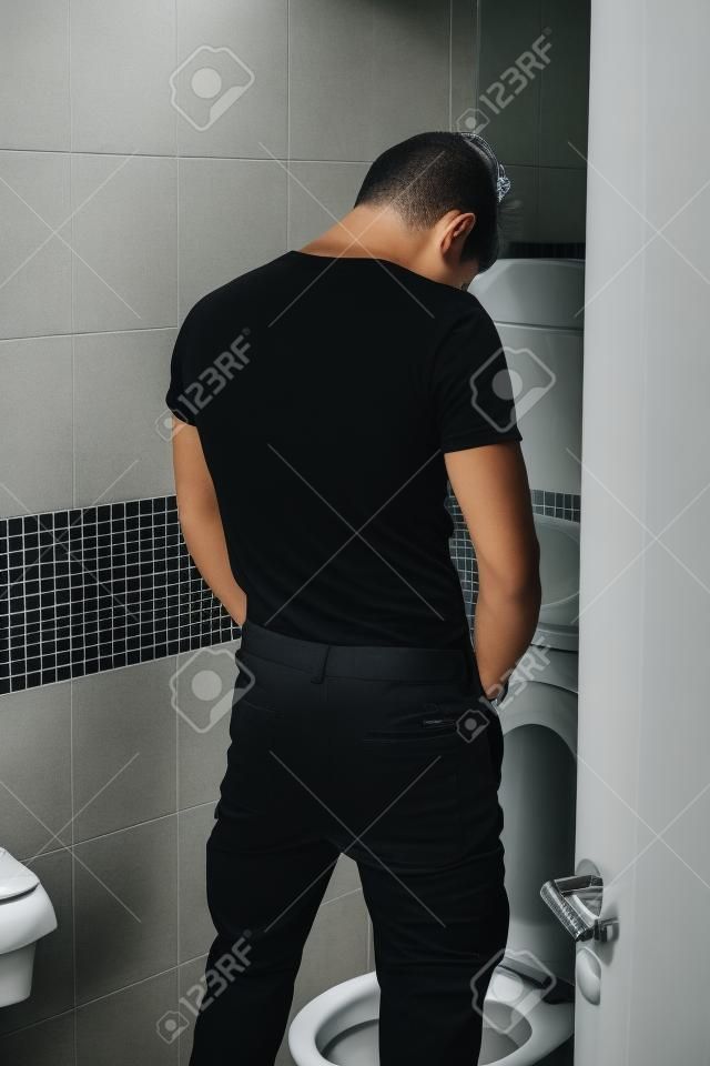Vista posterior de un hombre joven en traje Negro Orinar en el aseo interior de su baño.