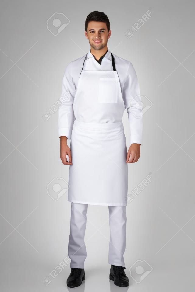 Długie strzał młody kucharz lub kelner pozowania, ma na sobie czarny fartuch i białą koszulę na białym tle