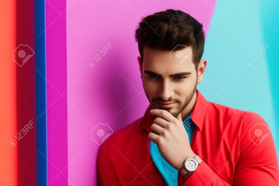 Attractive young man sitting against colorful wall, looking away to a side