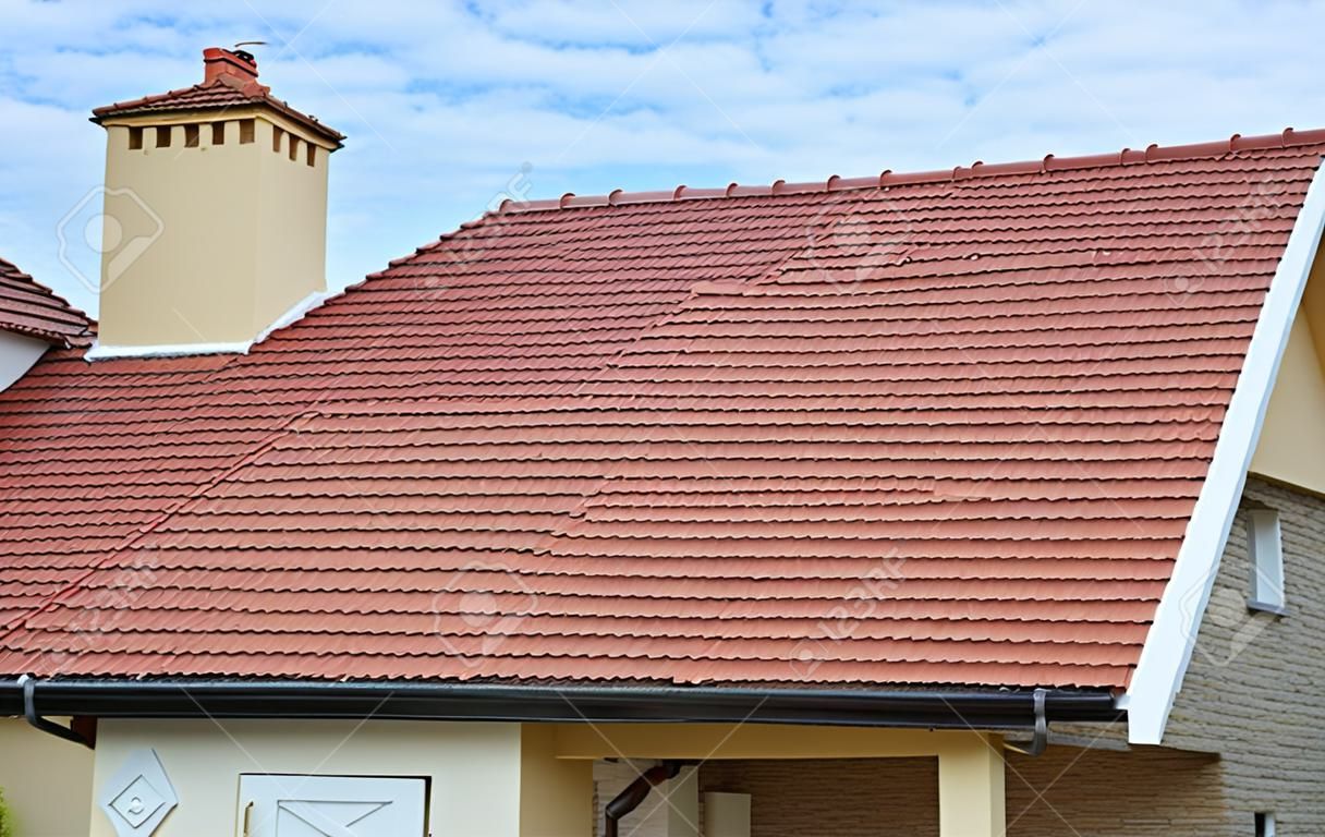 煙突、赤い粘土タイル張りの屋根と切り切れ屋根の構造の谷のタイプとモダンな家。屋根のデザインの異なるタイプと建物の屋根裏家の建設。屋根工事。