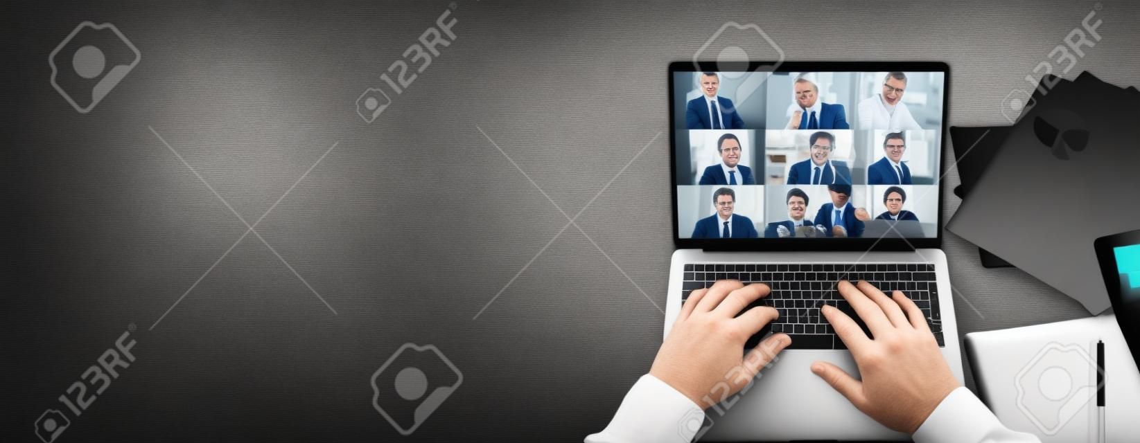 Vista superior da tela do laptop com participantes da videoconferência e mãos maduras do homem no teclado, laptop está em um desktop preto.