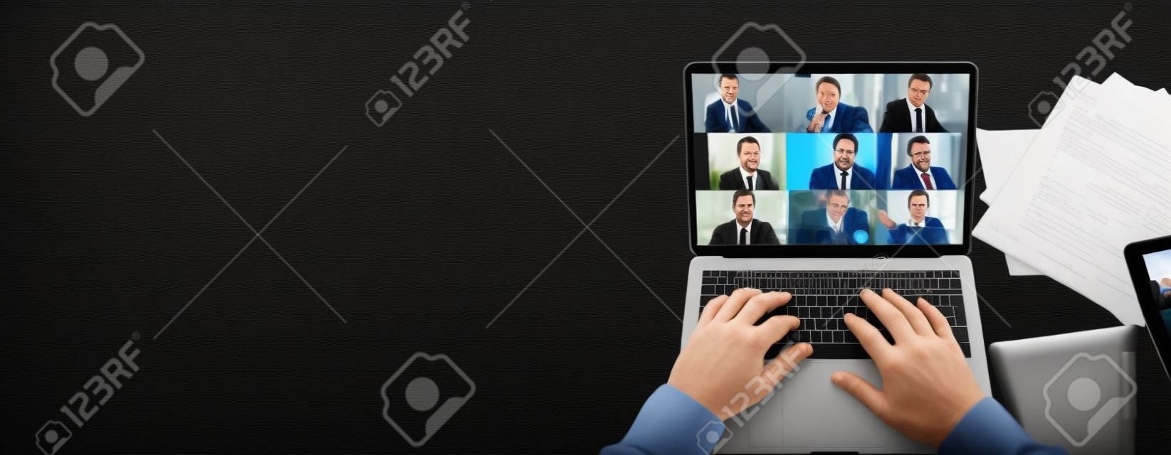 Vista superior da tela do laptop com participantes da videoconferência e mãos maduras do homem no teclado, laptop está em um desktop preto.