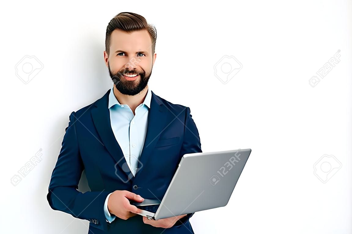 Portret pozytywnego odnoszącego sukcesy kaukaskiego brodatego biznesmena w garniturze, seo, konsultanta, brokera, stojącego na odizolowanym białym tle, trzymającego laptopa, patrzącego w kamerę, uśmiechającego się przyjaźnie