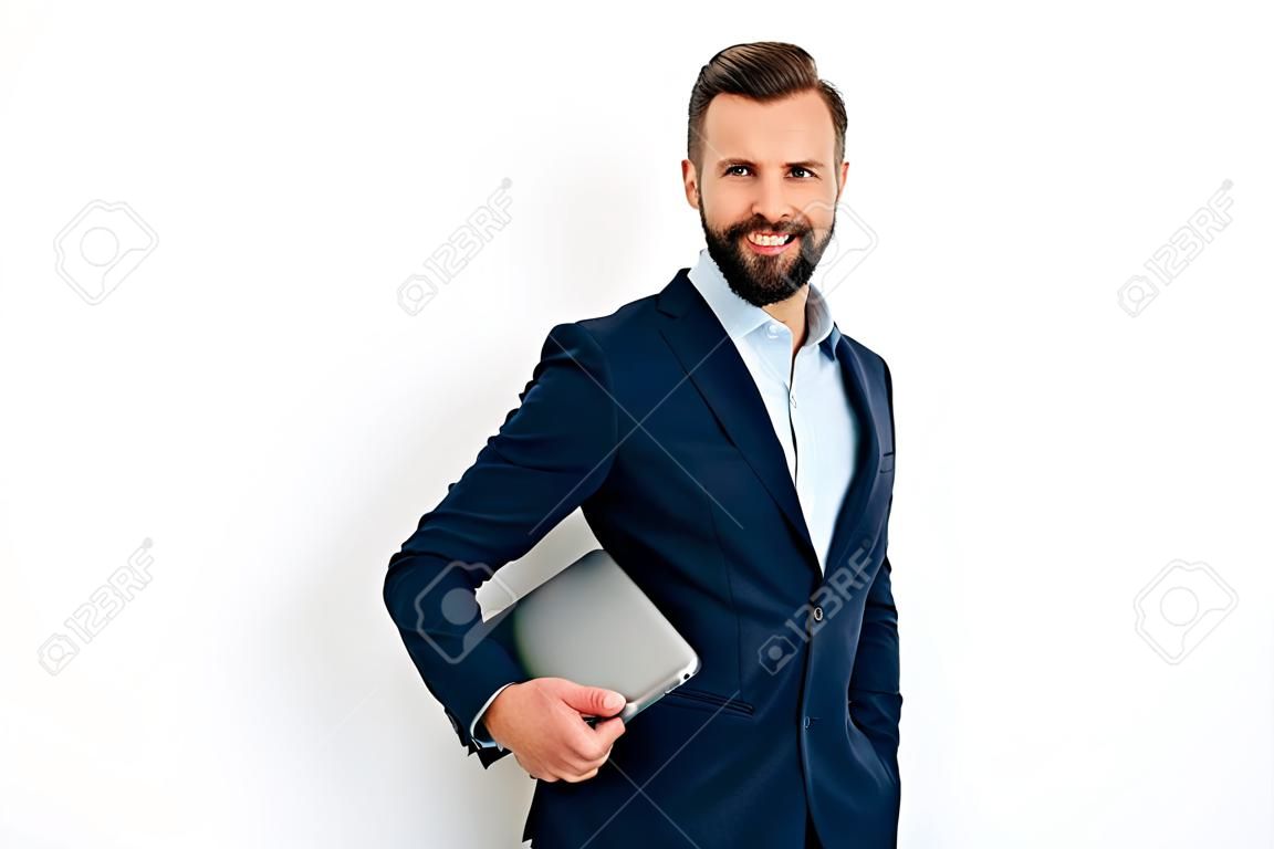 Portrait of a positive successful caucasian bearded business man in a suit, seo, consultant, broker, standing on isolated white background, holding laptop, looking at camera, smiling friendly