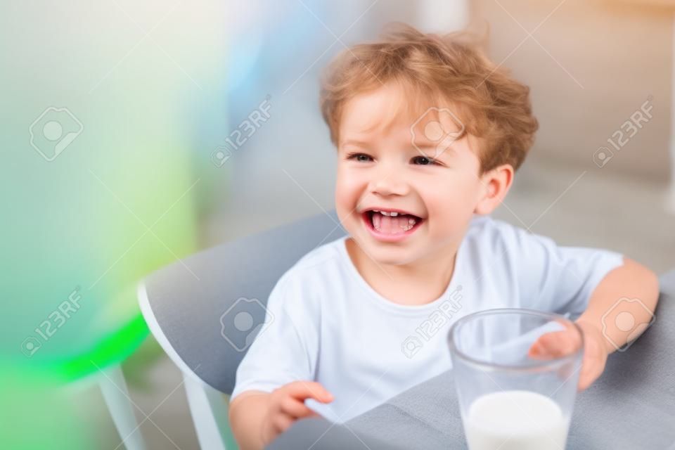 Il ragazzino si diverte a bere il latte in vetro trasparente con felicità.