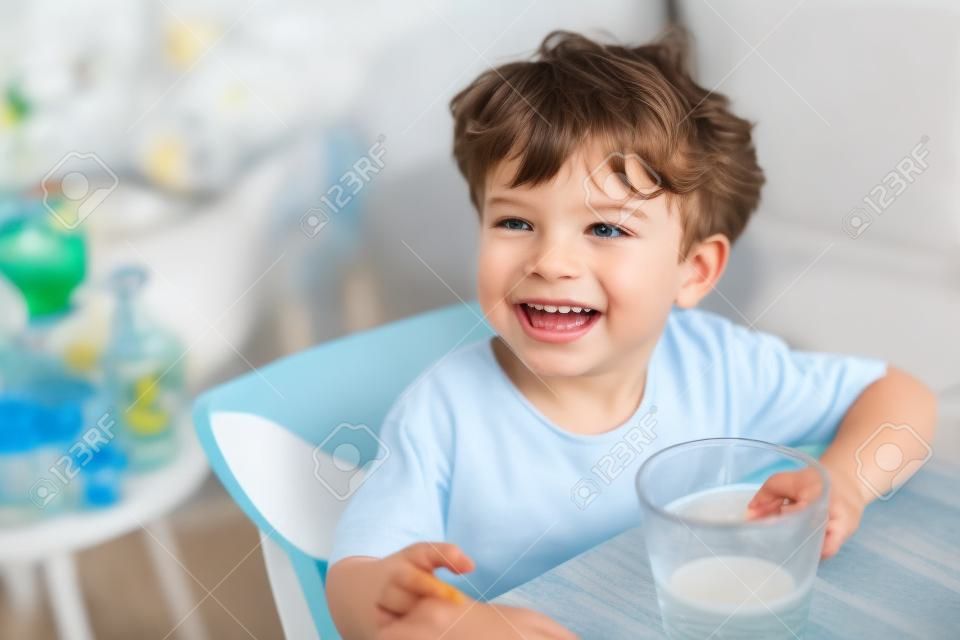 Il ragazzino si diverte a bere il latte in vetro trasparente con felicità.