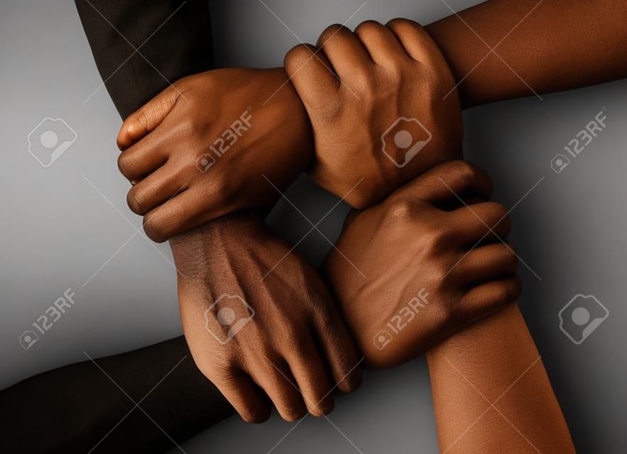 Grupo multirracial con manos negras afroamericanas caucásicas y asiáticas que sostienen la muñeca en la unidad de tolerancia, el amor y el concepto antirracismo aislado sobre fondo negro