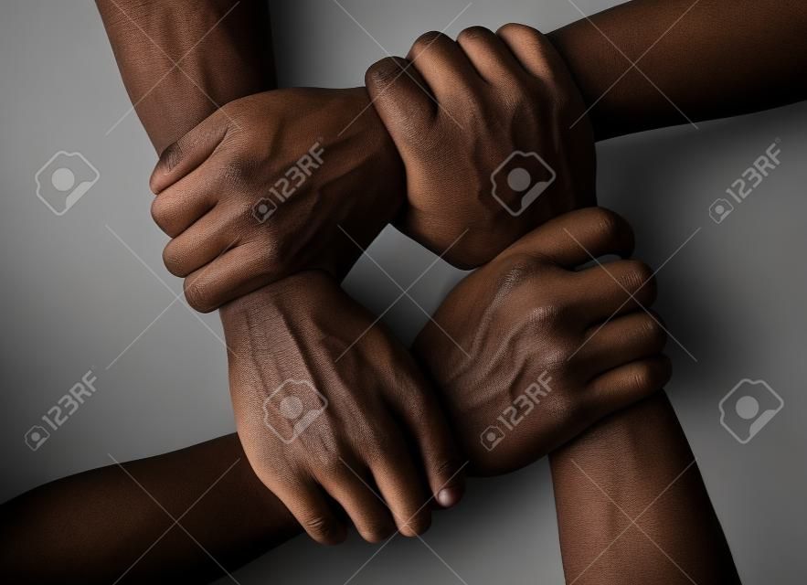 Multirassische Gruppe mit schwarzen afroamerikanischen, kaukasischen und asiatischen Händen, die sich gegenseitig am Handgelenk in Toleranz, Einheitsliebe und Antirassismuskonzept auf schwarzem Hintergrund halten