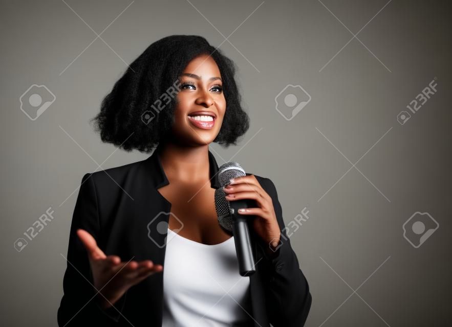 Joven mujer de negocios afroamericana negra atractiva y segura con micrófono hablando en auditorio en evento corporativo o seminario dando motivación y conferencia de coaching de éxito