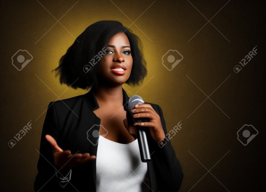 młoda atrakcyjna i pewna siebie czarna afroamerykańska kobieta biznesu z mikrofonem przemawiającym w audytorium na imprezie firmowej lub seminarium, dając motywację i sukces konferencji coachingowej