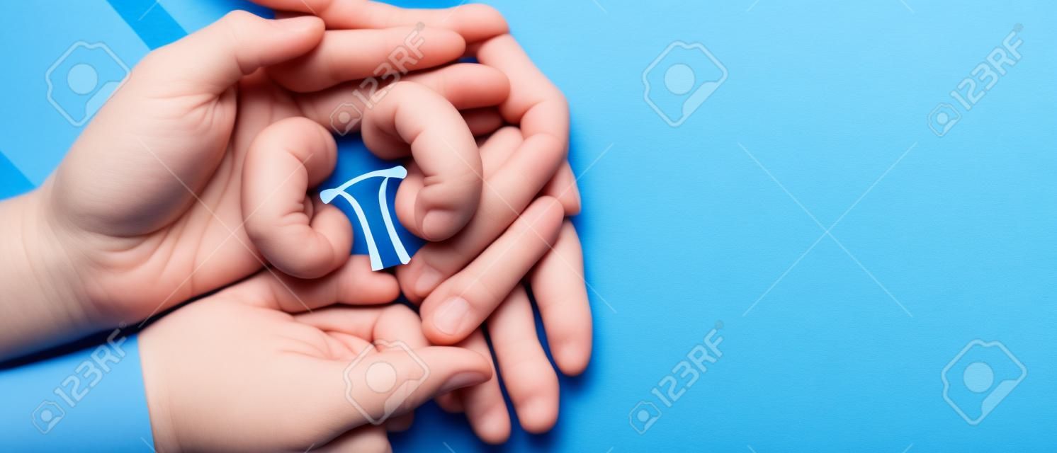 Adult and child holding kidney shaped paper on textured blue background, world kidney day, National Organ Donor Day, charity donation concept