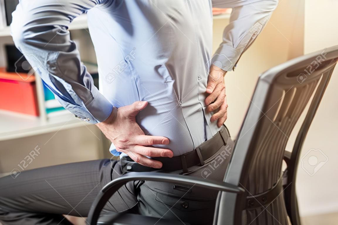 Businessman suffering from back pain in office, light effect