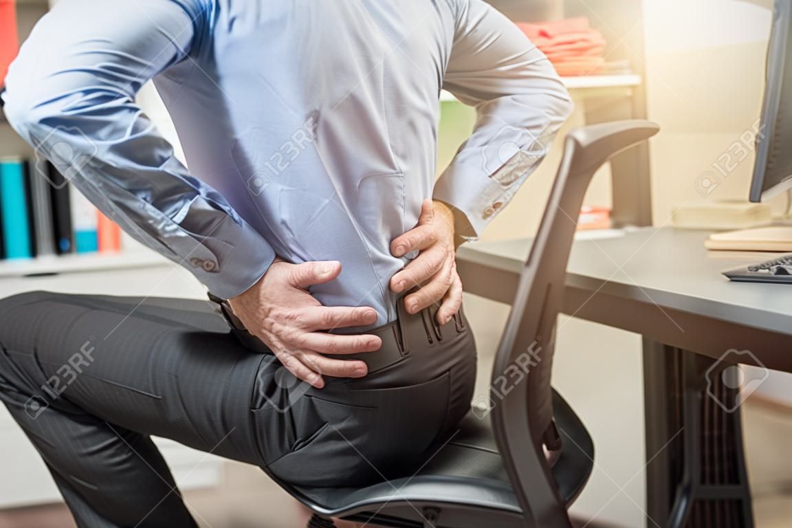 Businessman suffering from back pain in office, light effect