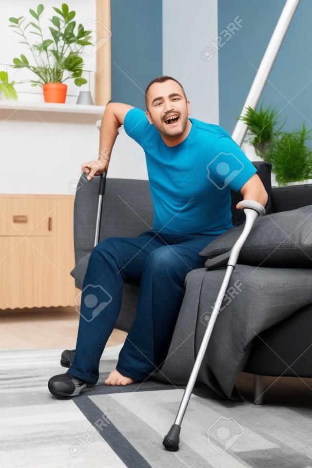 Un hombre con una pierna rota intenta ponerse de pie con muletas de un sofá