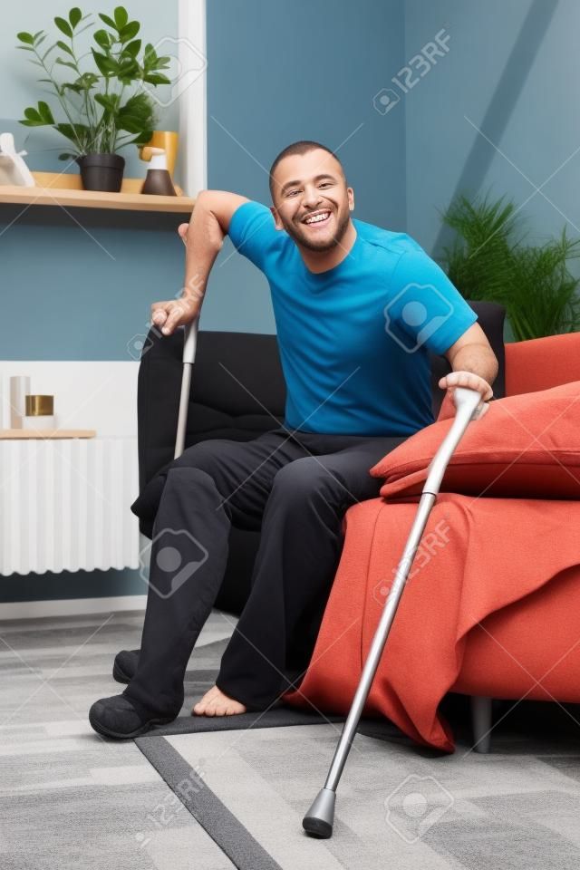 Un hombre con una pierna rota intenta ponerse de pie con muletas de un sofá