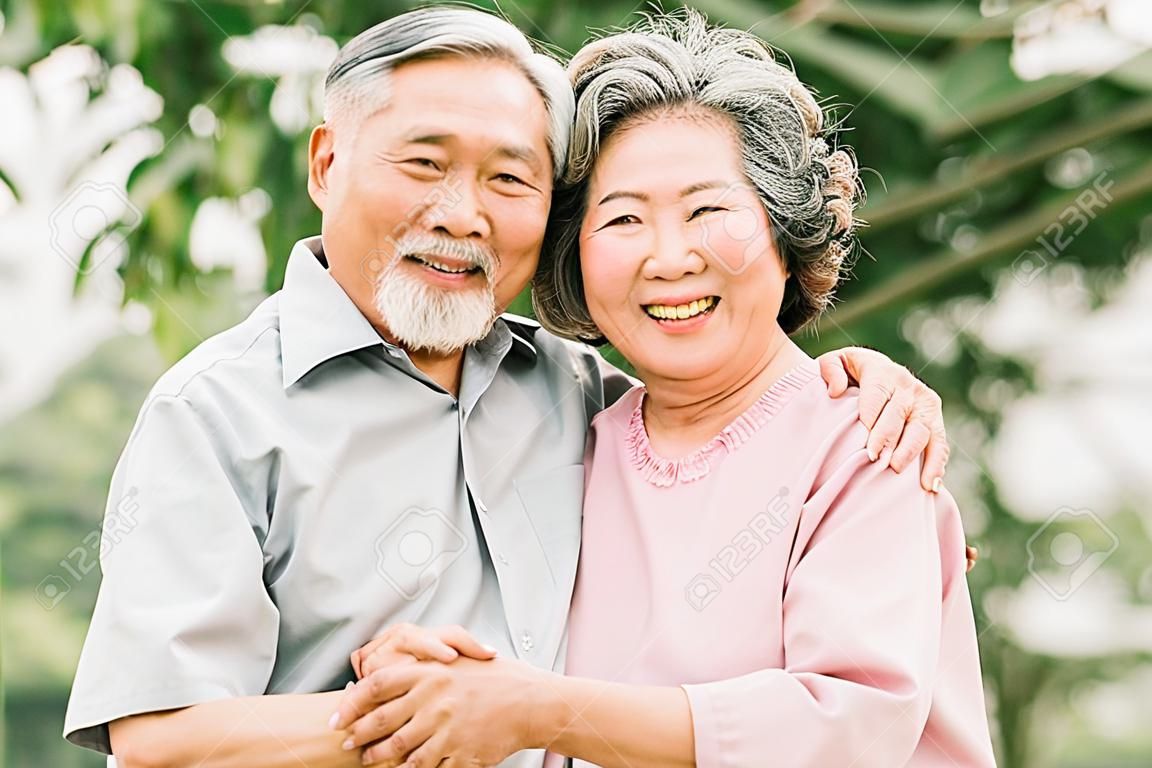 Feliz casal sênior asiático sorrindo enquanto se abraçam ao ar livre no parque.
