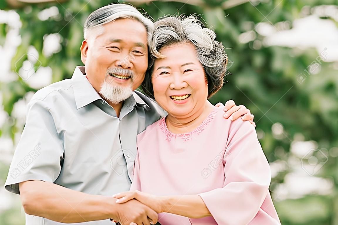 Happy Asian senior couple smiling while holding each other outdoor in the park.