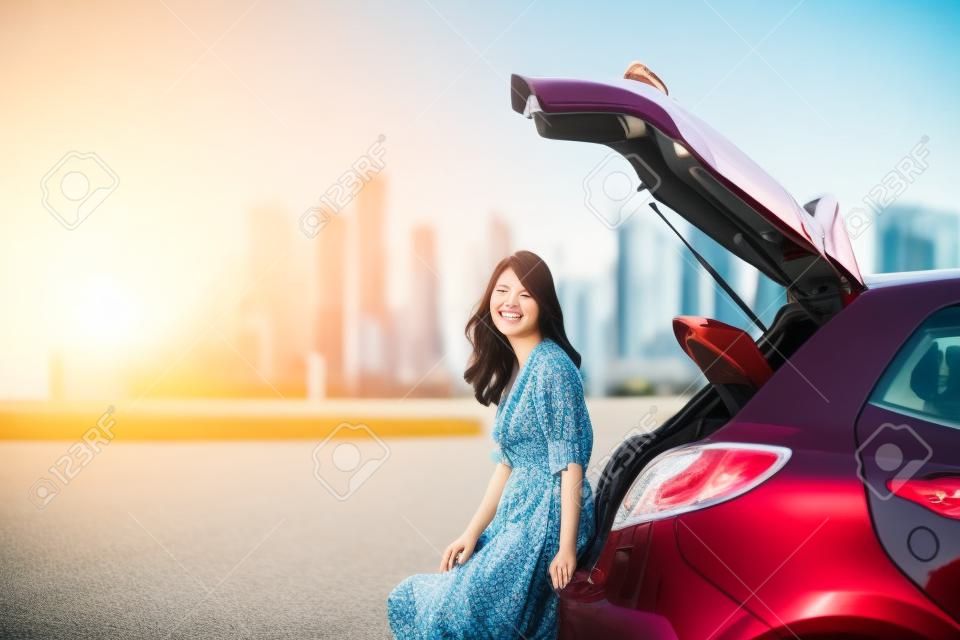 Viaggiatore asiatico felice della donna che si siede sul bagagliaio dell'auto durante le vacanze