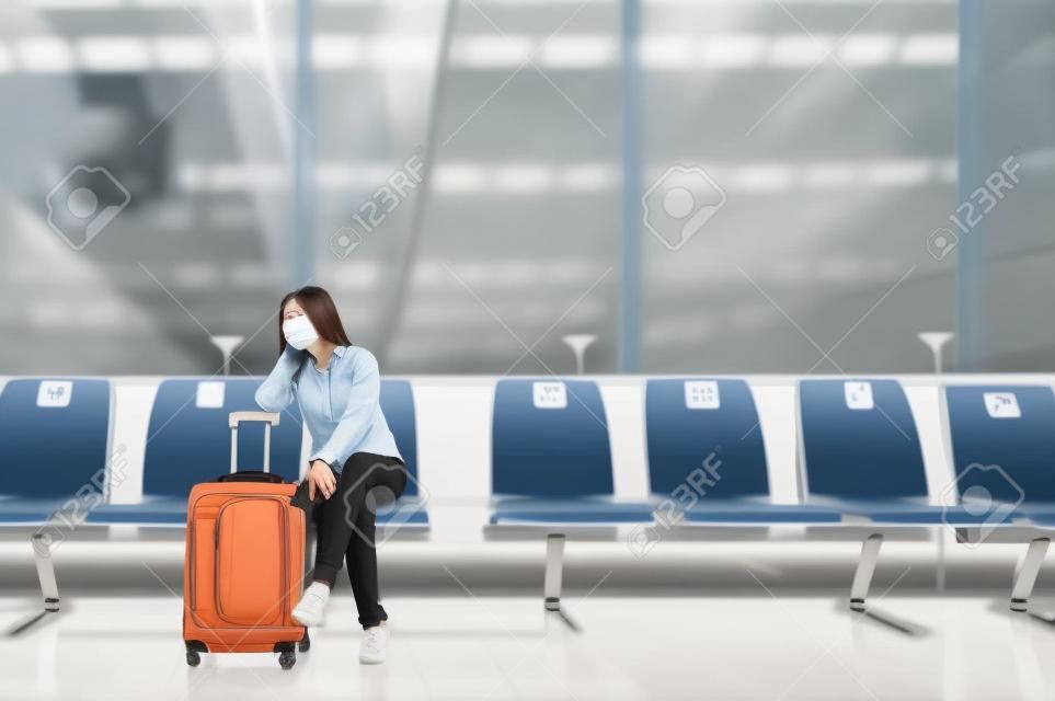 Asiatische touristin mit gesichtsmaske sitzt auf einem sozial distanzierenden stuhl mit gepäck und wartet auf den flug am flughafenterminal während des ausbruchs von coronavirus oder covid-19. Neue normale Reise am Flughafen