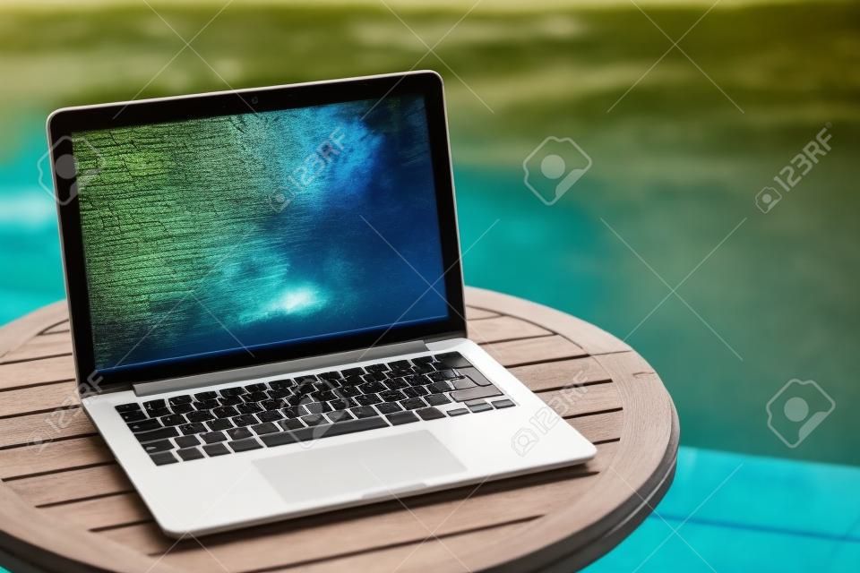 laptop on a wooden table against the background of accepted Swimming pool