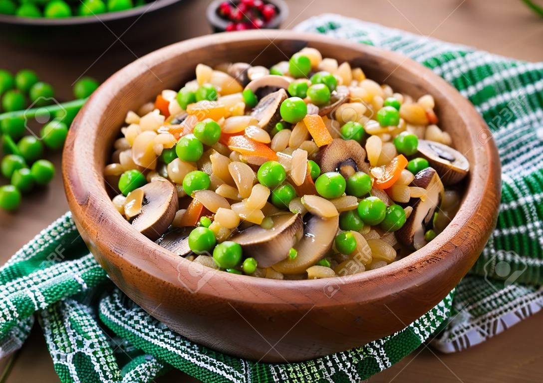 Vegetarian crumbly pearl barley porridge with mushrooms and green peas in a wooden bowl